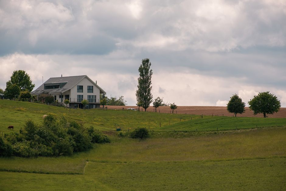 A modern house nestled in a lush green countryside under a cloudy sky.