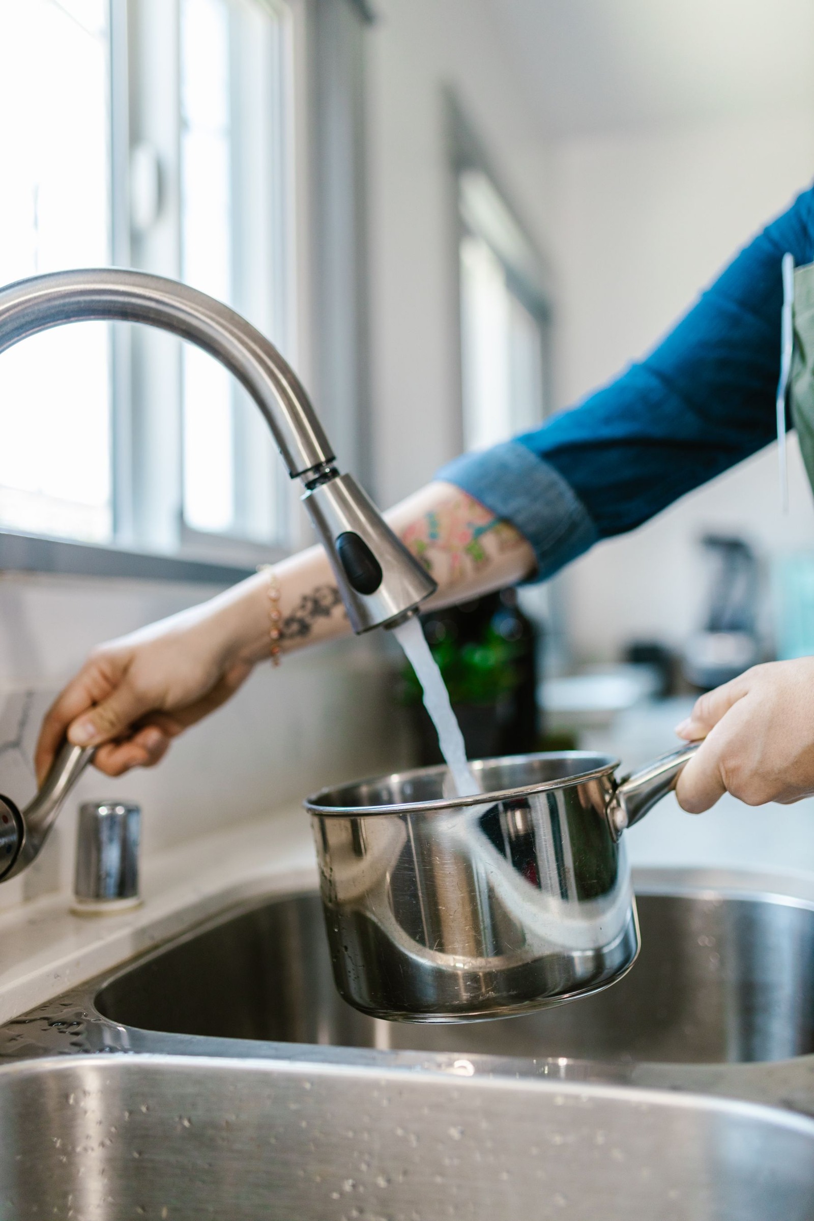 Hand filling a stainless steel cooking pot with tap water