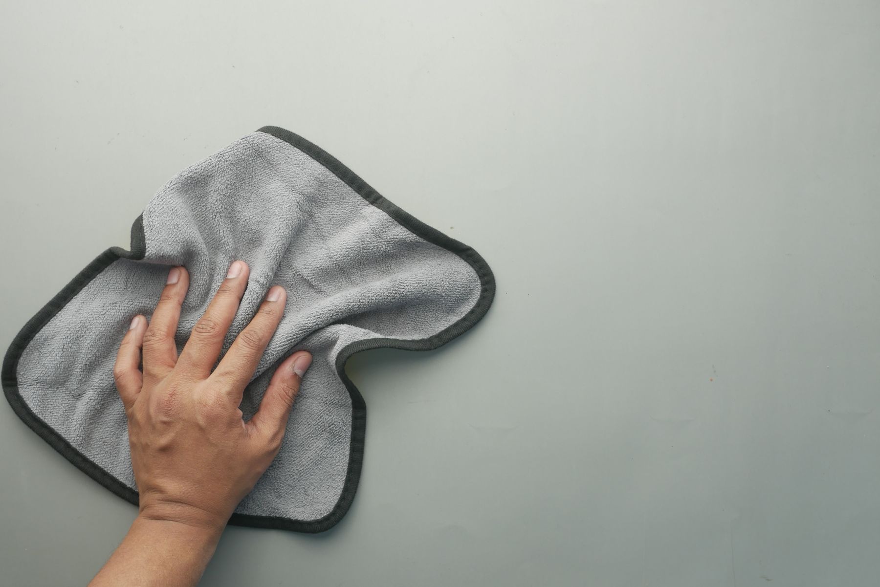 Hand wiping a light-colored table with a gray microfiber cloth