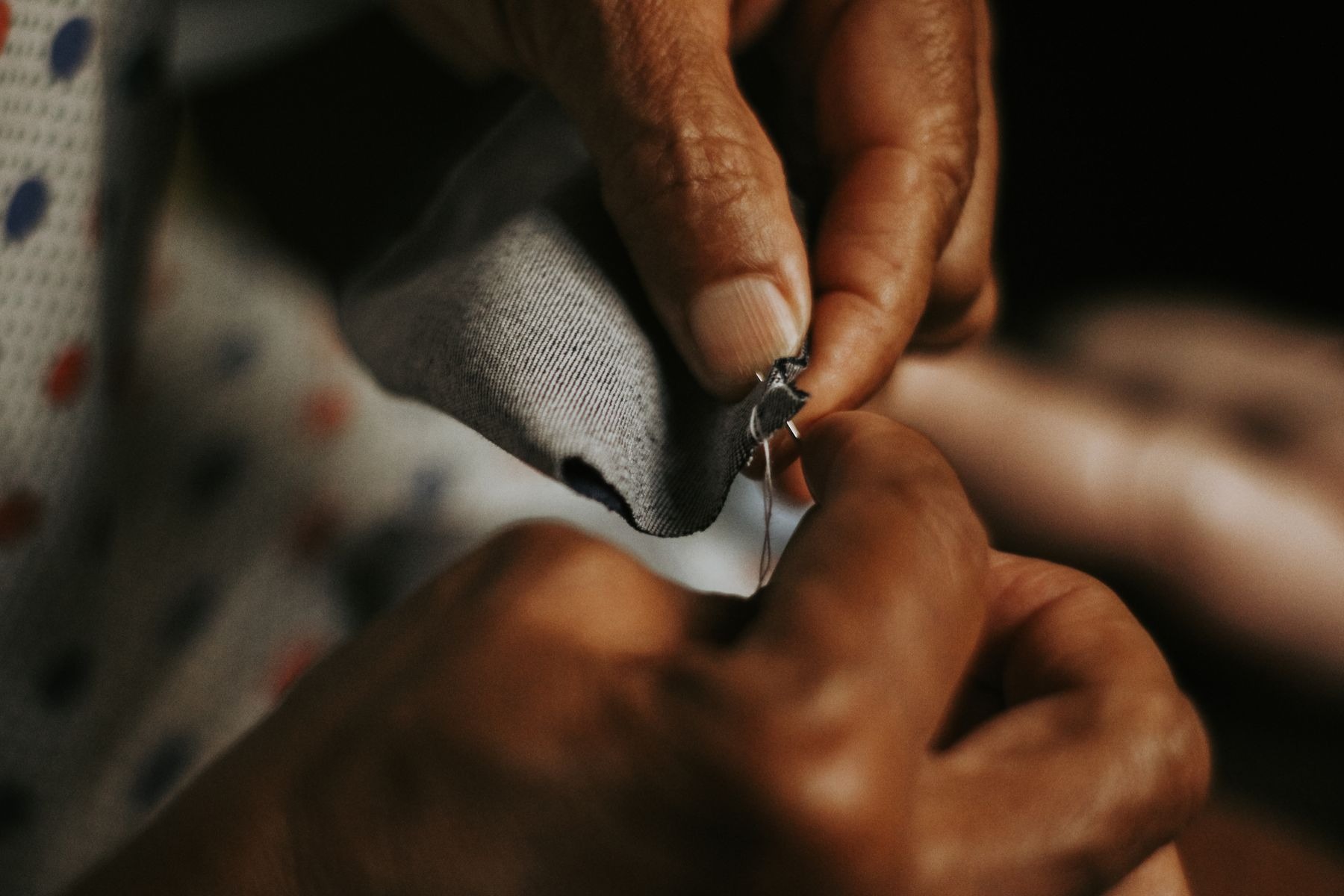 Close view of hands sewing gray fabric with a needle and thread