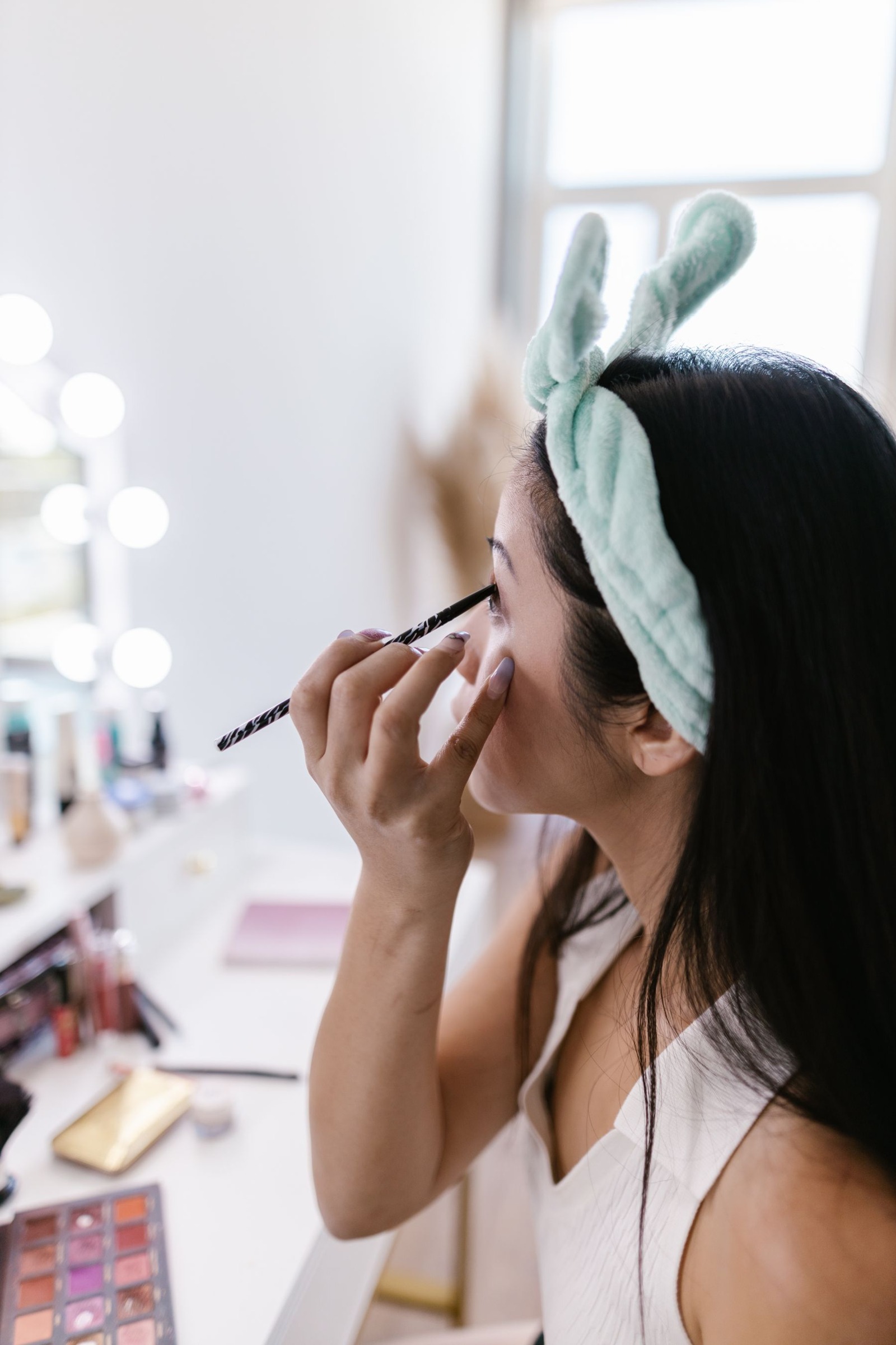 Woman looking in a mirror while filling her eyebrows with a pencil