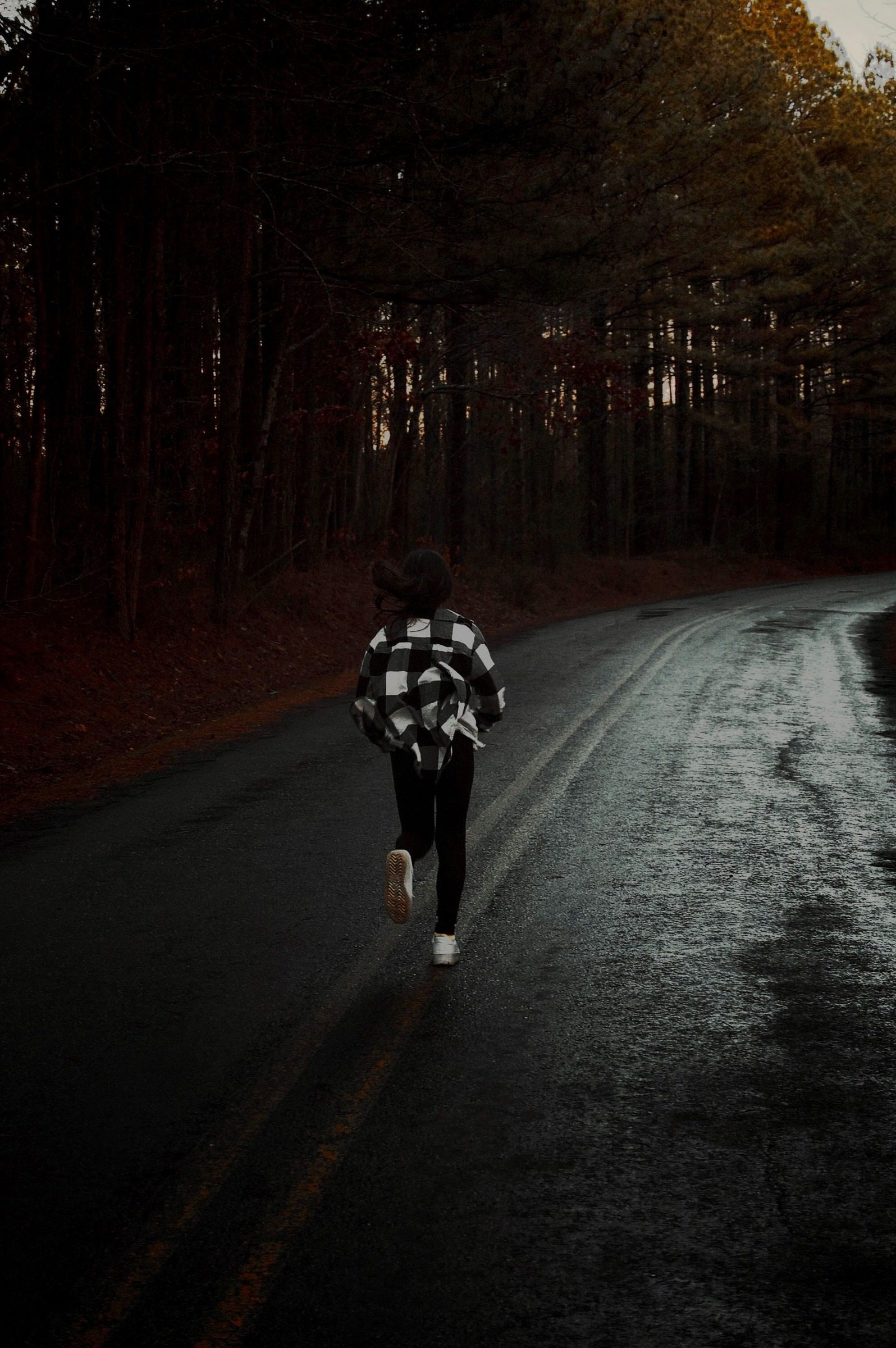 Rear view of a person running along a wet forest road after rain