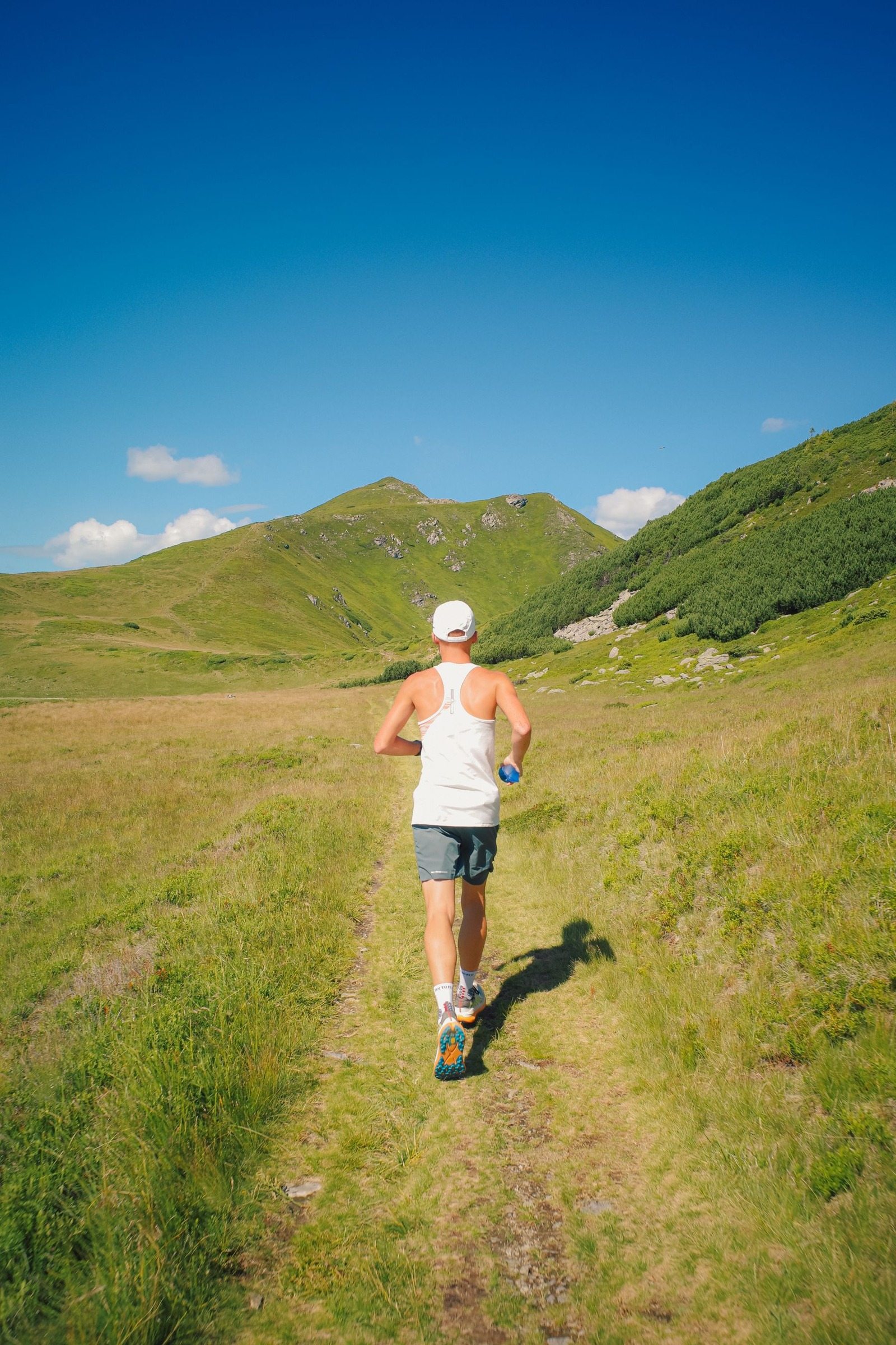 Rear view of a man running along a sunny mountain trail