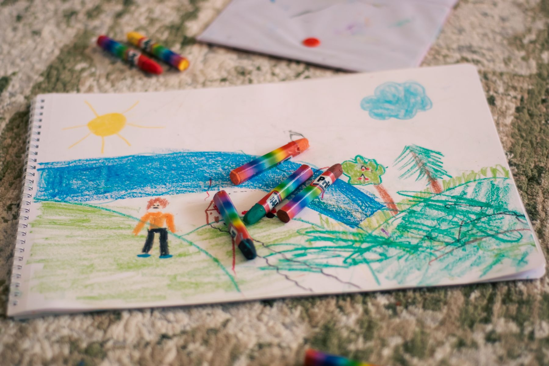 Child's landscape drawing with crayons scattered on the paper