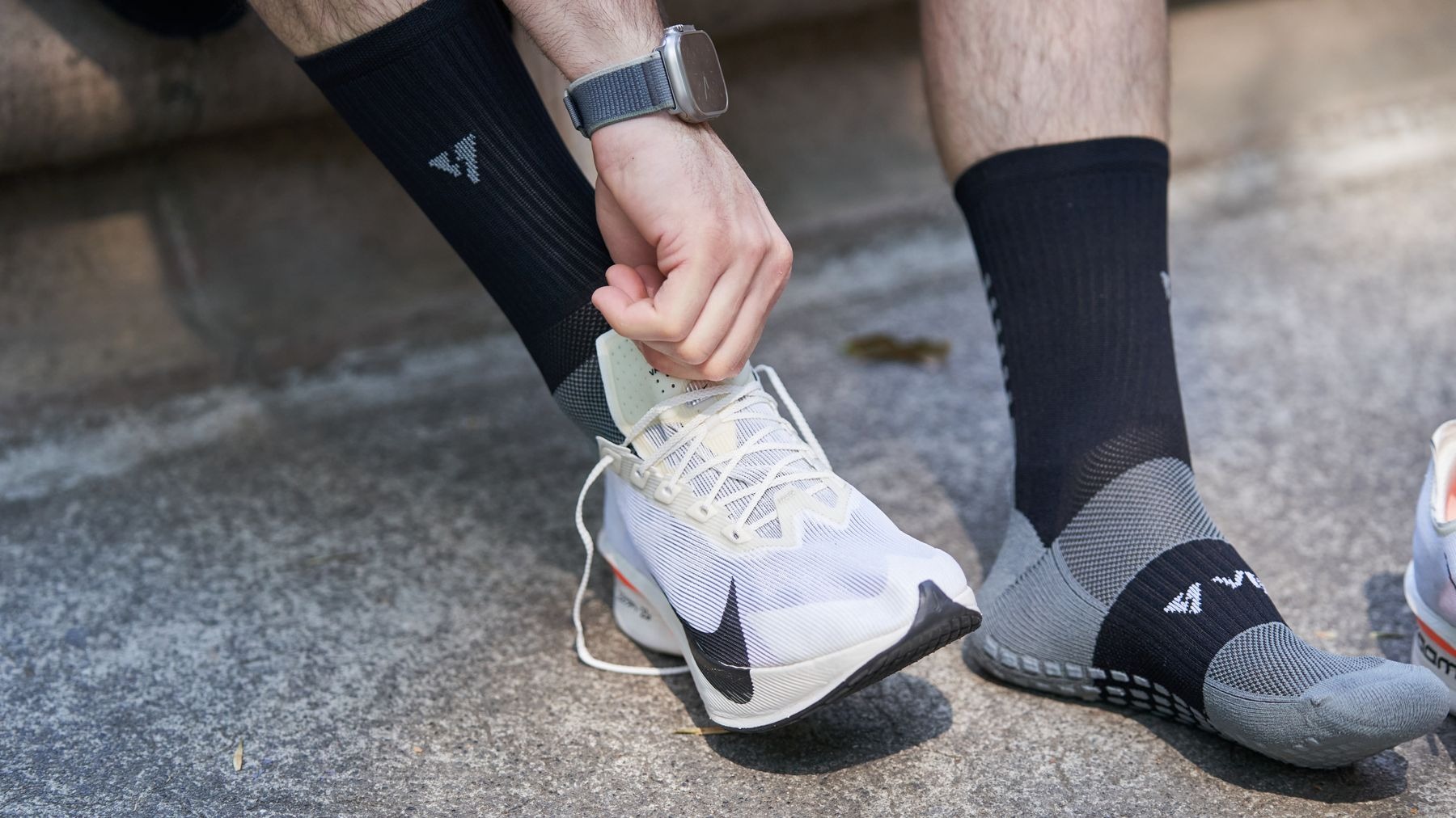 Man tying his running shoe laces outdoors in sunlight