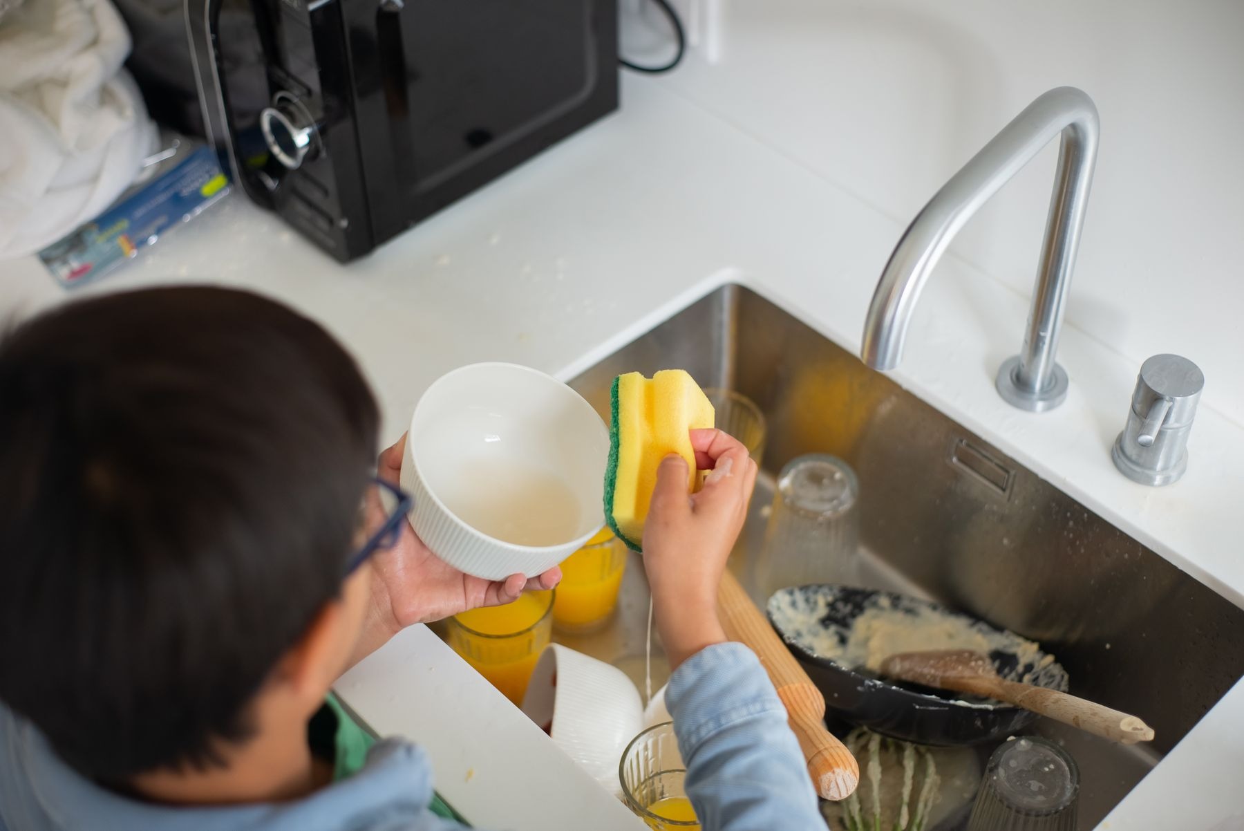 Young boy washing dishes with a sponge at a kitchen sink