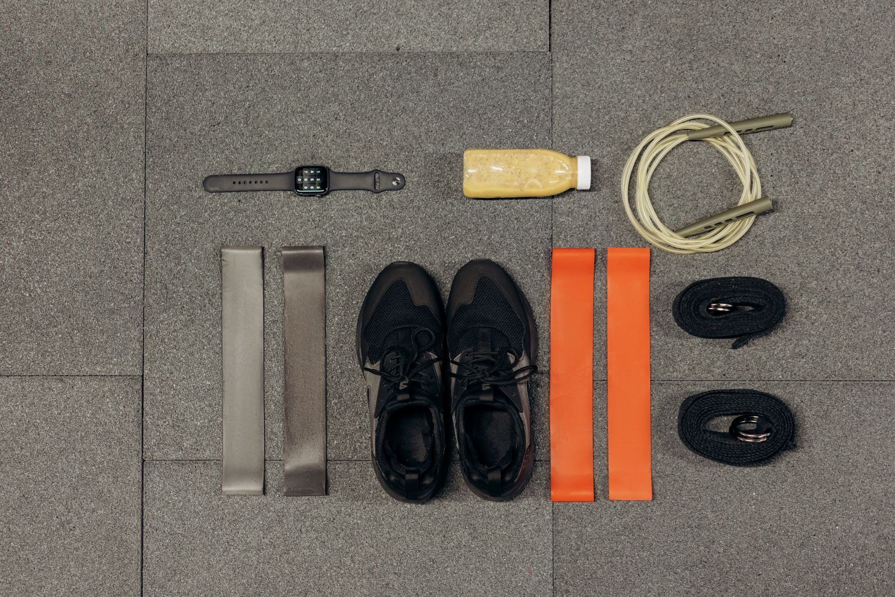 Workout shoes, resistance bands, watch and rope arranged on a gray surface