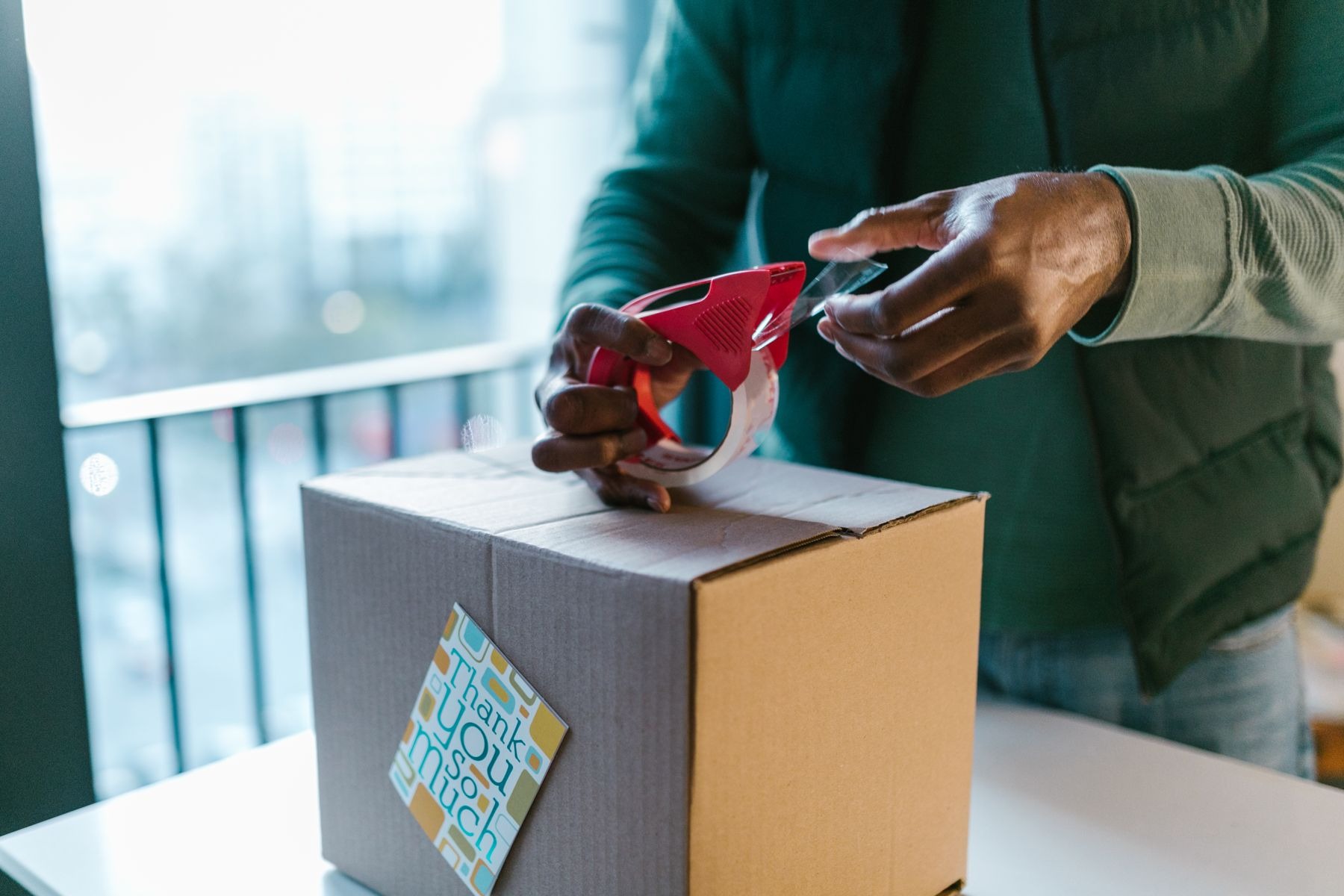 Close view of a person sealing a cardboard box with a tape dispenser