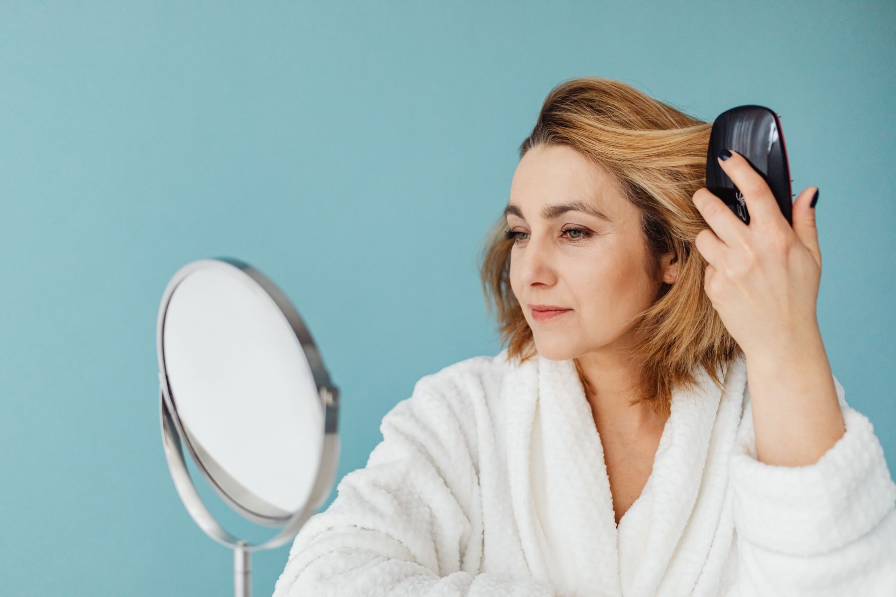 Woman in a bathrobe combing her hair in front of a mirror