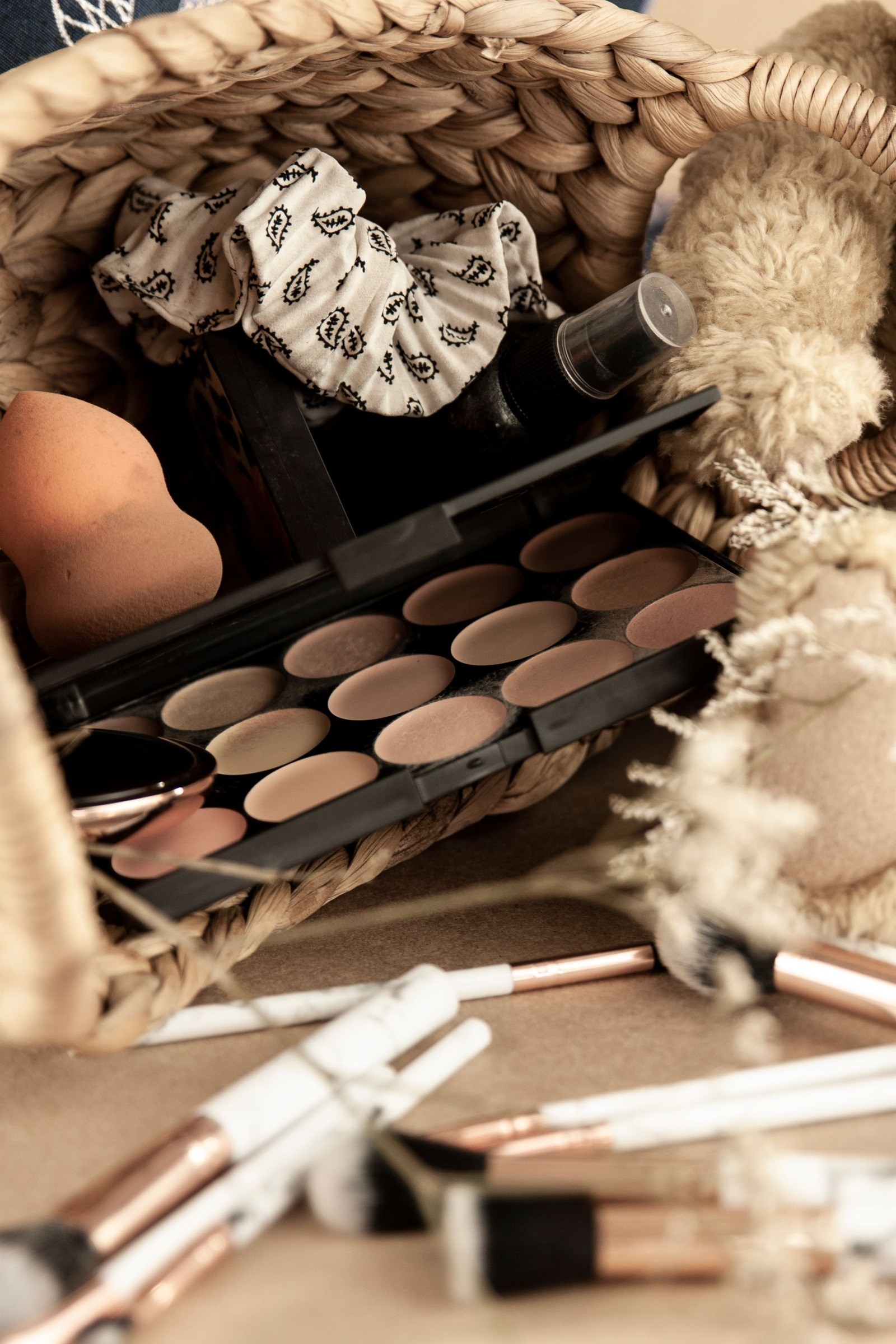 Cosmetic bag, makeup products, brushes and a scrunchie arranged on a table