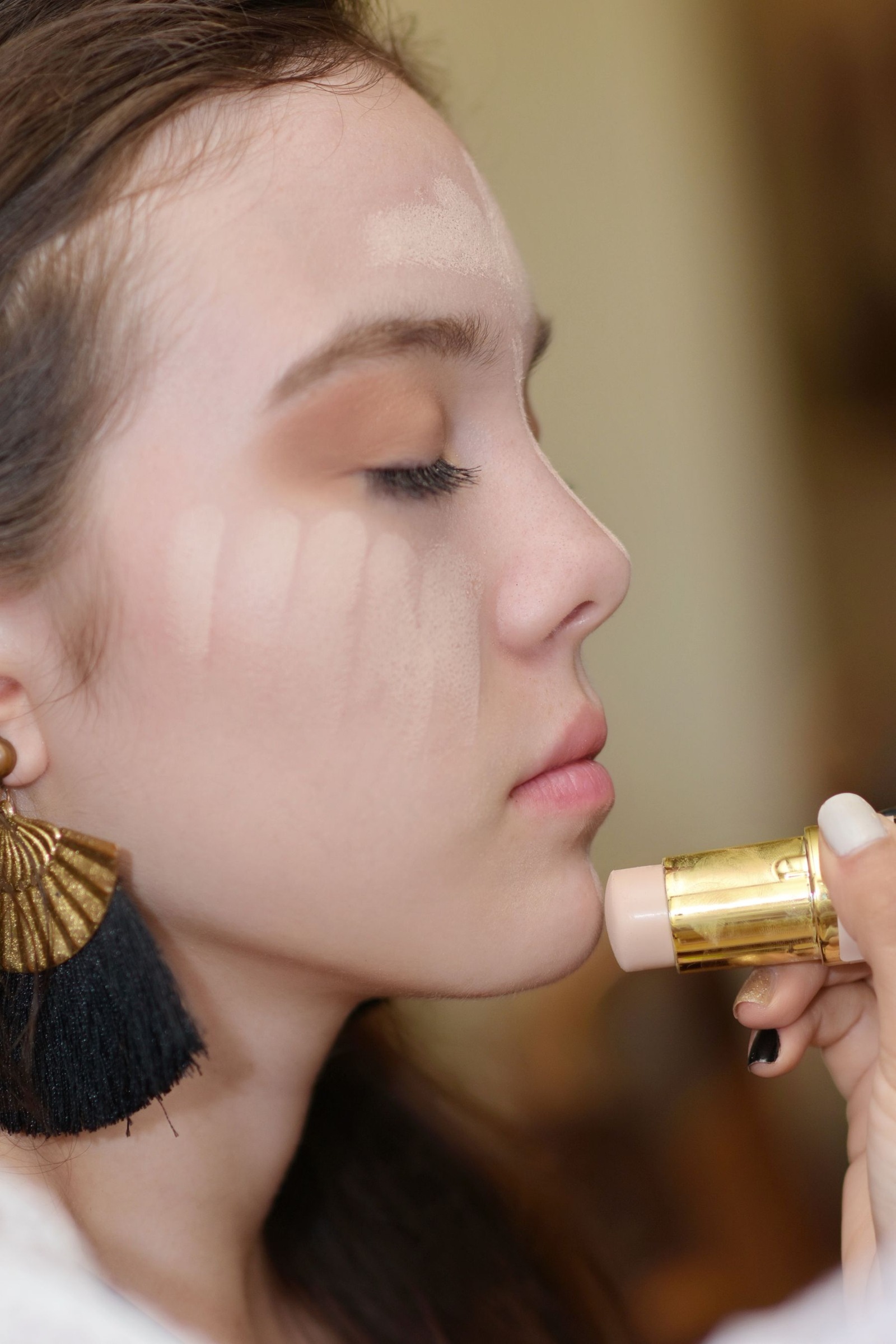Side view of a woman applying concealer makeup with her eyes closed