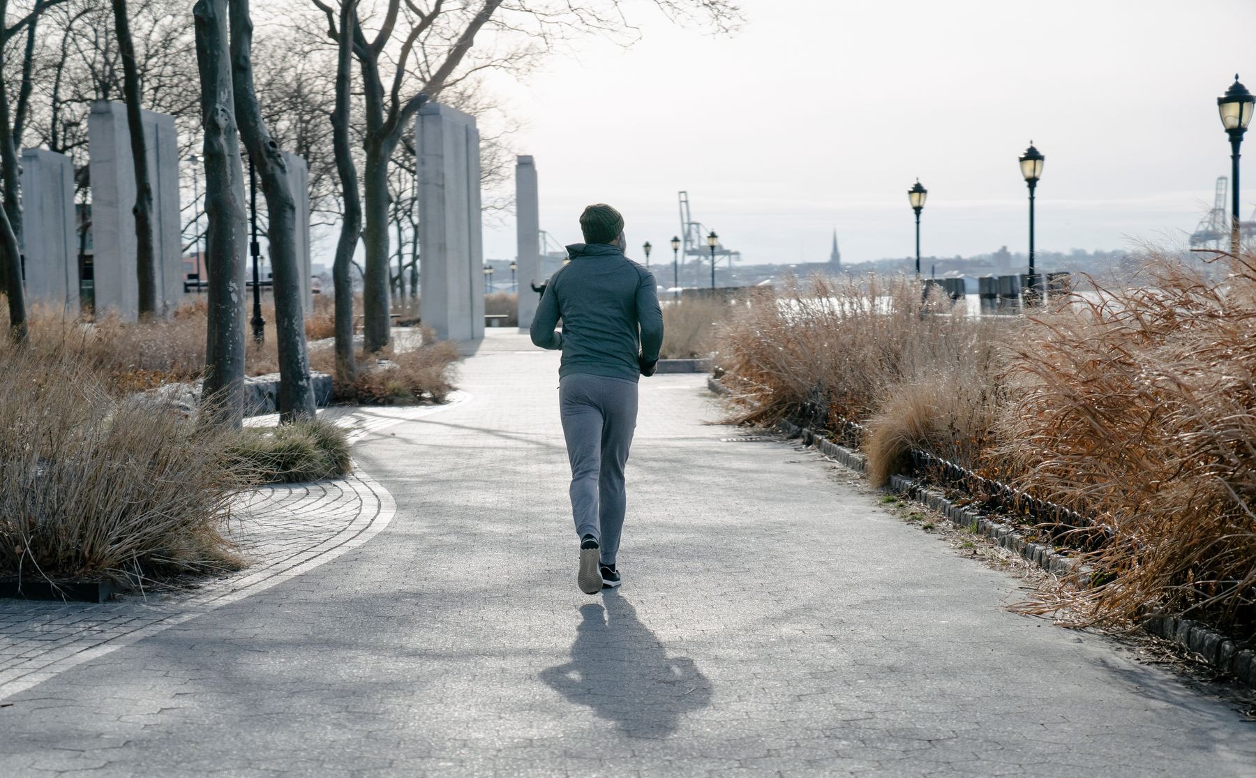 Rear view of a man in a knitted hat jogging on an autumn park walkway