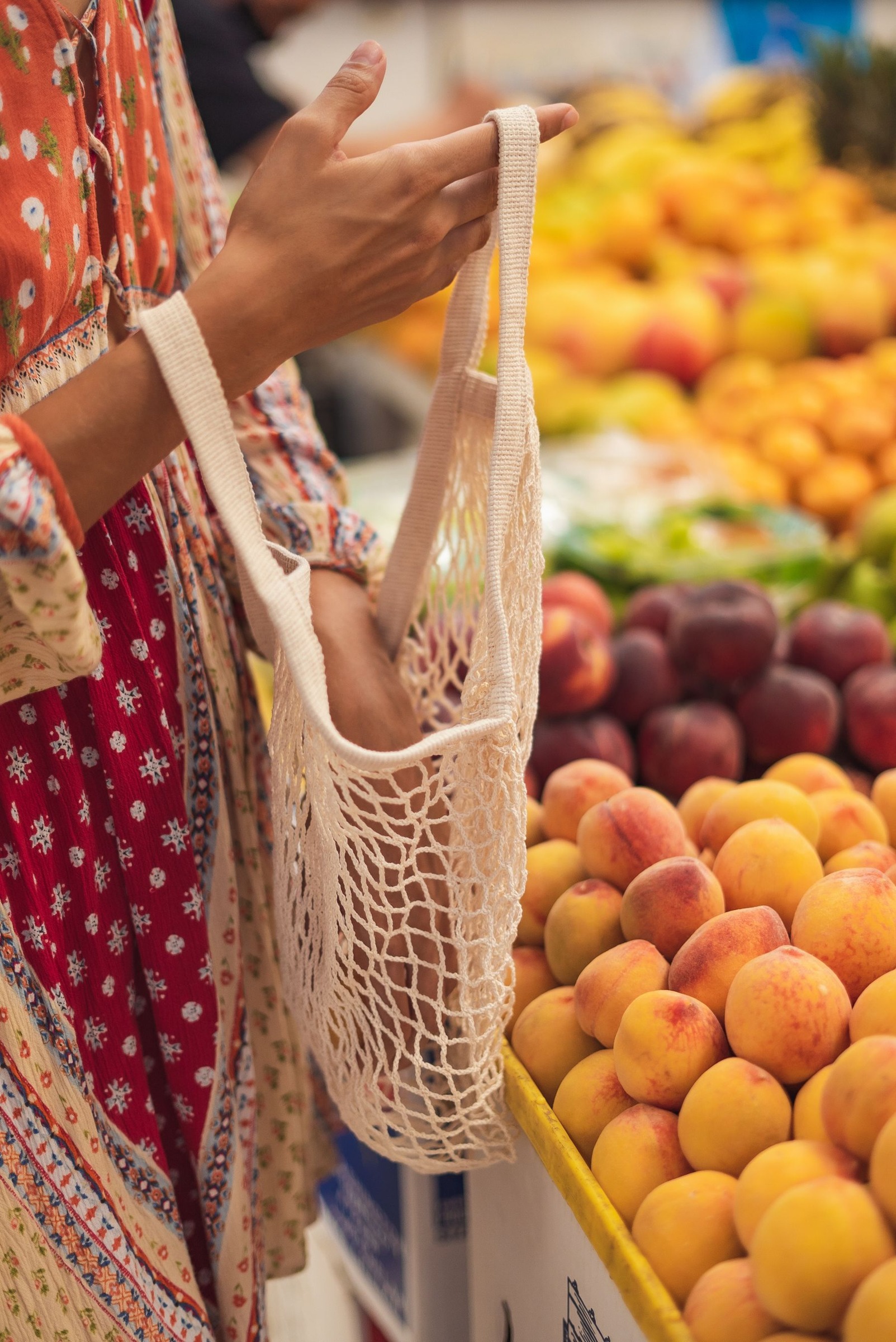 Woman holding a reusable shopping bag beside a fruit stall