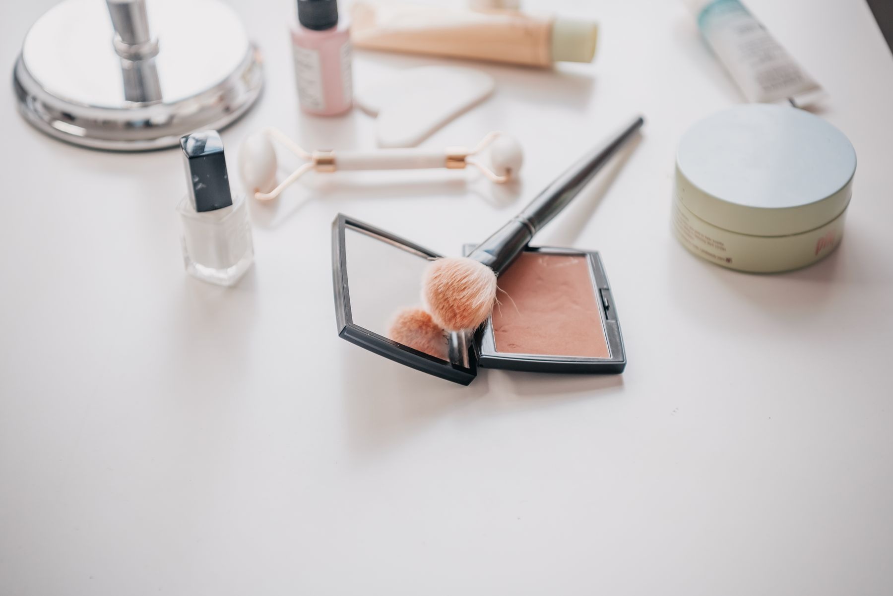Makeup brush resting on a compact mirror among cosmetics on a vanity