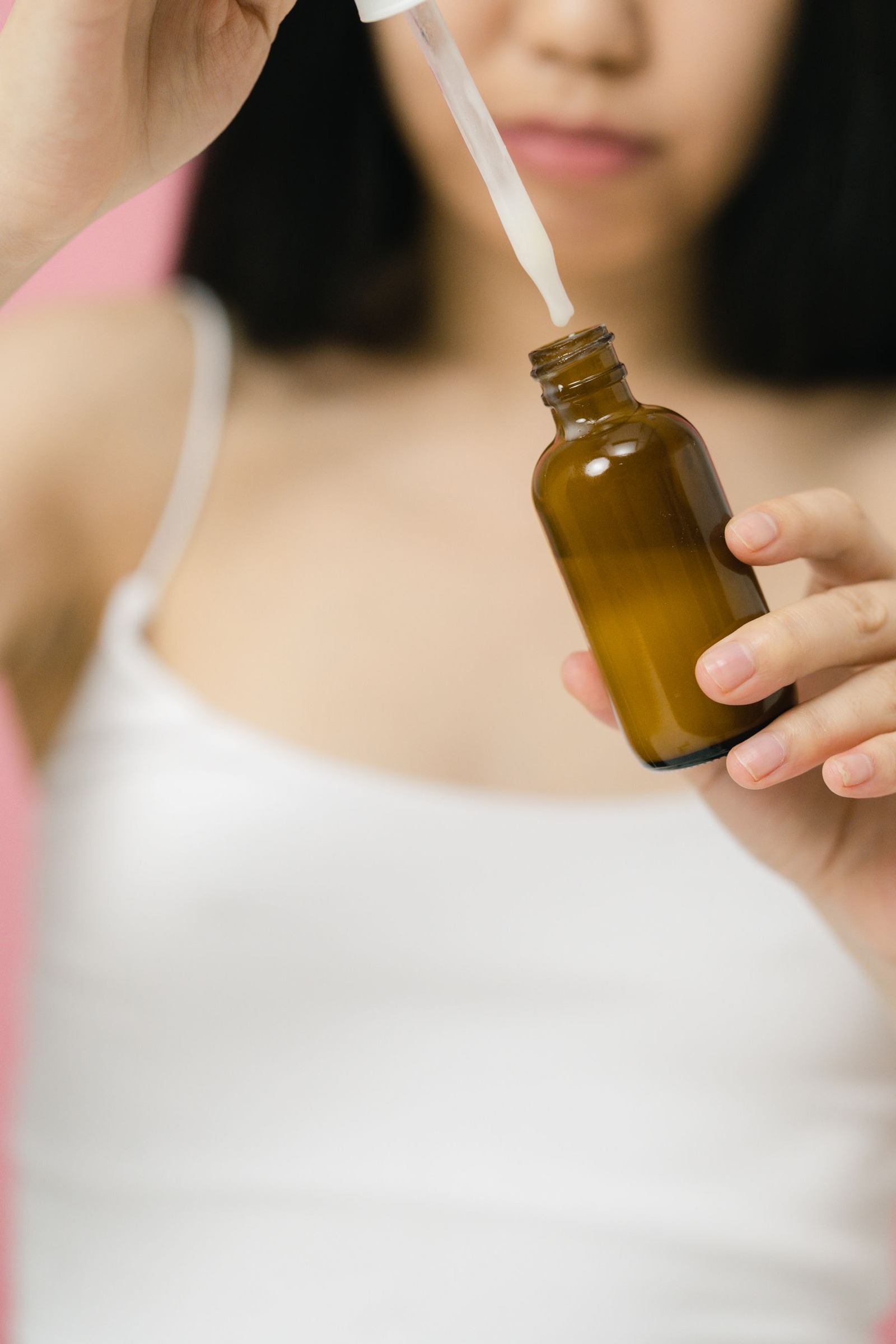 Woman in a white tank top holding a serum bottle and pipette