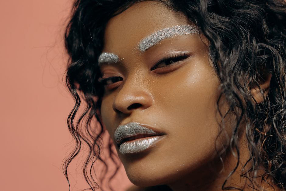 Detailed portrait of a woman with silver glitter makeup and curly hair on a pink backgroun