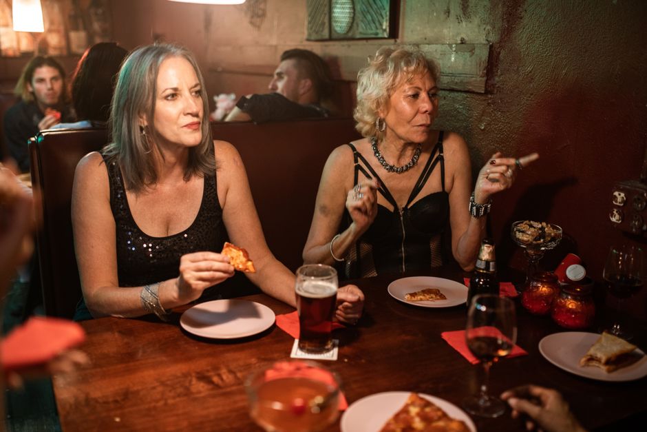 Two women enjoying beer, pizza, and conversation in a cozy restaurant setting.